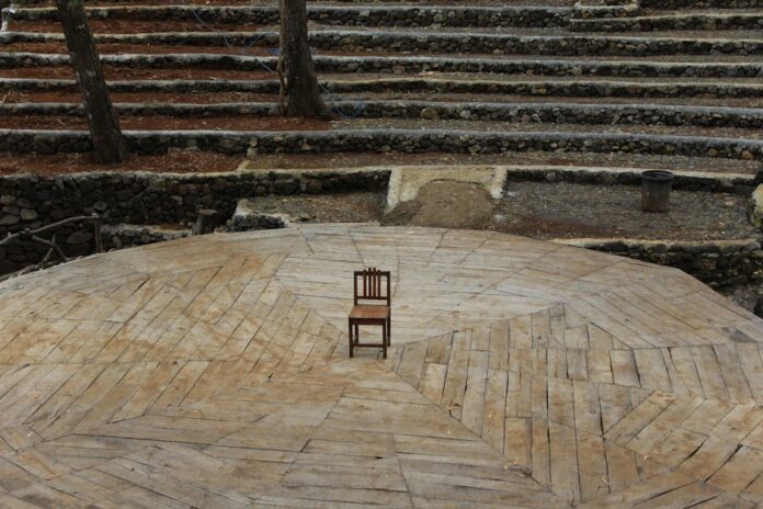 störtebeker festspiele - Lone wooden chair on an amphitheater stage surrounded by trees.